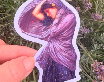 Puede incluir: Una pegatina troquelada con la reproducción de una pintura de una persona de cabello oscuro, que lleva un pañuelo morado fluido y una prenda oscura estampada. La persona tiene un brazo levantado hacia la cabeza y una pequeña flor amarilla.