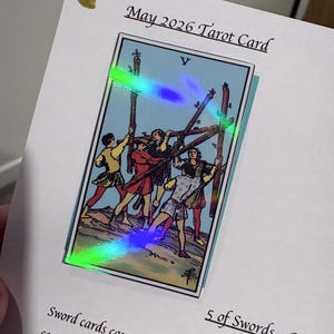 Pu&ograve; includere: Una carta bianca con il testo May 2026 Tarot Card e 5 of Swords - Reverse. Al centro &egrave; presente un'illustrazione della carta dei tarocchi Cinque di Bastoni con una sovrapposizione olografica che mostra cinque figure che tengono bastoni. Un piccolo cuore dorato &egrave; in alto a sinistra.