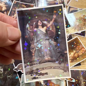 Puede incluir: Una pegatina rectangular con una superposici&oacute;n de estrellas hologr&aacute;ficas sobre una pintura cl&aacute;sica de una figura con vestiduras drapeadas sentada en un trono. La figura sostiene un c&aacute;liz con un brazo levantado. Tiene un borde blanco.