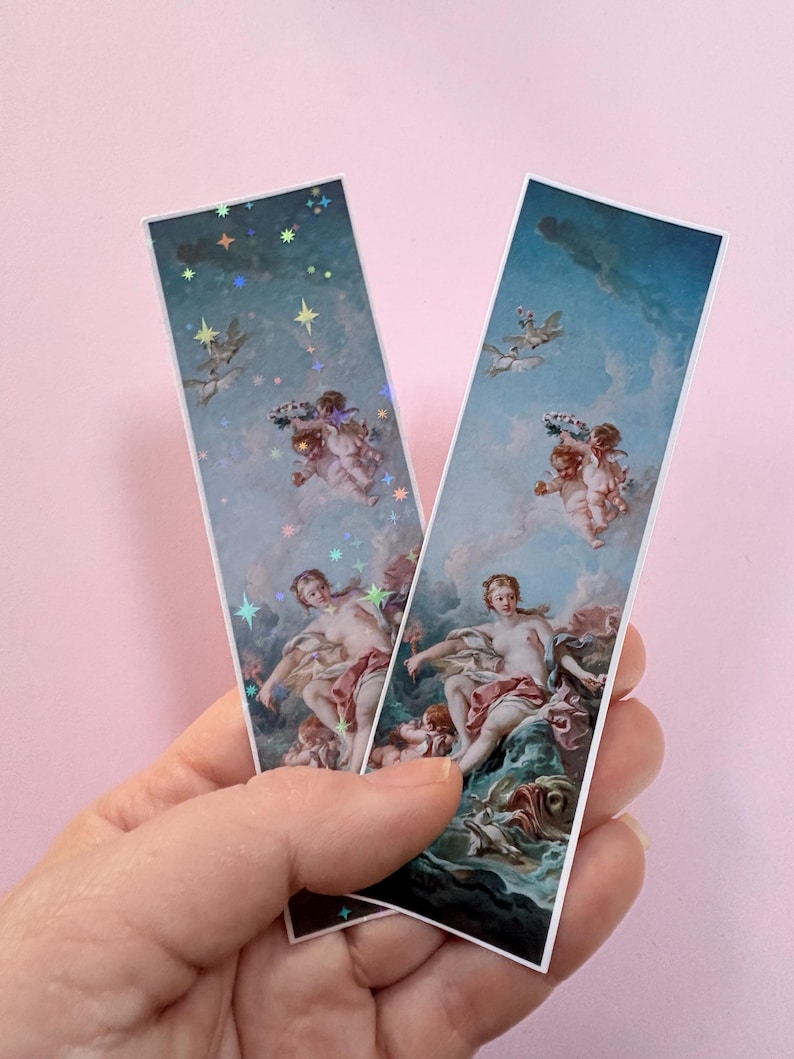 以下が含まれることがあります： 雲と青空の中に横たわる人物と天使が描かれた古典的な絵画の長方形のしおり2枚。左側のしおりにはホログラムの星模様が重ねられており、右側のしおりには星模様のない同じ絵柄が描かれています。