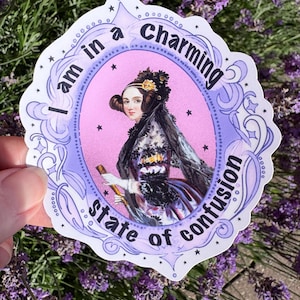 May include: A die-cut sticker featuring a portrait of a person in historical attire within a purple ornate frame. The text "I am in a charming state of confusion" is printed in black along the border. The background inside the frame is pink.
