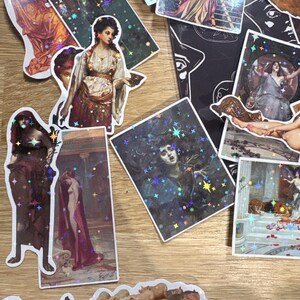 Puede incluir: Una colecci&oacute;n de pegatinas rectangulares y troqueladas con reproducciones de arte cl&aacute;sico y una capa de estrellas hologr&aacute;ficas. Las pegatinas muestran varias figuras con vestimenta hist&oacute;rica, escenas mitol&oacute;gicas y un grupo de cerdos con acabado brillante.