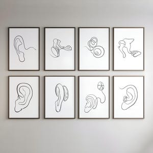 Può includere: Otto stampe artistiche incorniciate con disegni a linea minimalisti dell'orecchio umano e delle sue strutture interne. L'arte lineare nera è ambientata su uno sfondo bianco, con cornici marrone scuro. L'opera d'arte è esposta su una parete grigio chiaro.