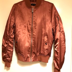 May include: A brown satin bomber jacket with a zip closure and two pockets. The jacket has a ribbed collar, cuffs, and hem.