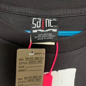 May include: A black t-shirt with a white graphic print of a skull and crossbones. The tag on the shirt reads "Saint" and "100% Cotton Extra Heavyweight Made in Japan".