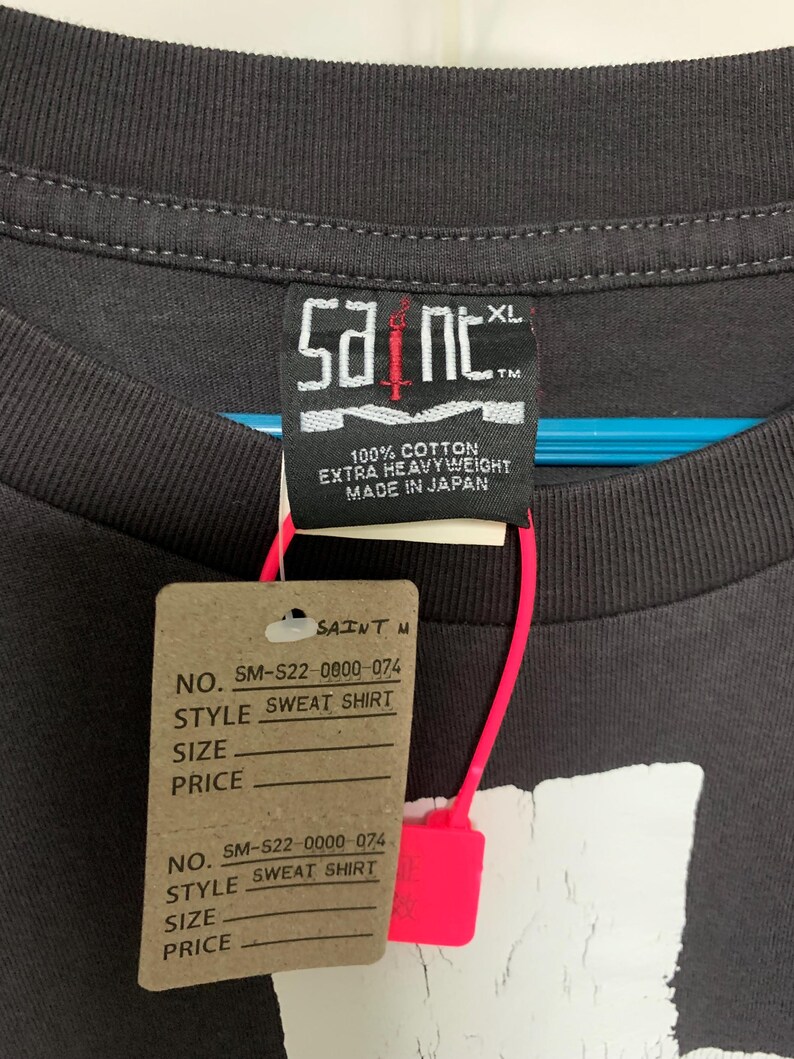 May include: A black t-shirt with a white graphic print of a skull and crossbones. The tag on the shirt reads "Saint" and "100% Cotton Extra Heavyweight Made in Japan".