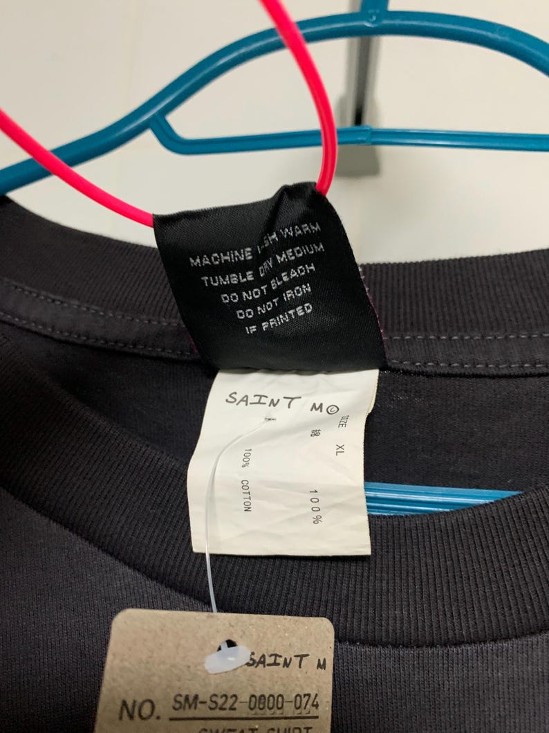 May include: Black t-shirt with a white tag that says "SAINT MO" and "100% COTTON". The tag also has a size label that says "XL". There is a smaller tag that says "SAINT M" and "NO. SM-S22-0000-074".