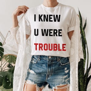May include: White t-shirt with black text that reads "I knew u were trouble" with the word "trouble" in red.