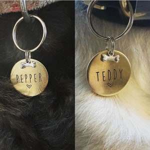 May include: Two gold dog tags with bone and heart charms. The tag on the left says "Pepper" and the tag on the right says "Teddy".