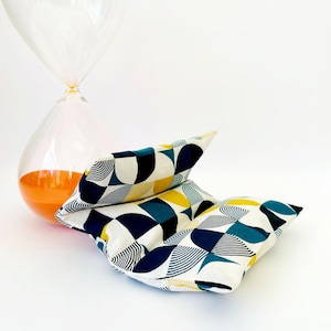 May include: A pair of white fabric cushions with a geometric pattern in shades of blue, teal, and yellow. The cushions are folded in half and are lying on a white surface.