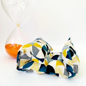 May include: A white, blue and yellow geometric patterned pillow. The pillow is made of fabric and is folded in half.