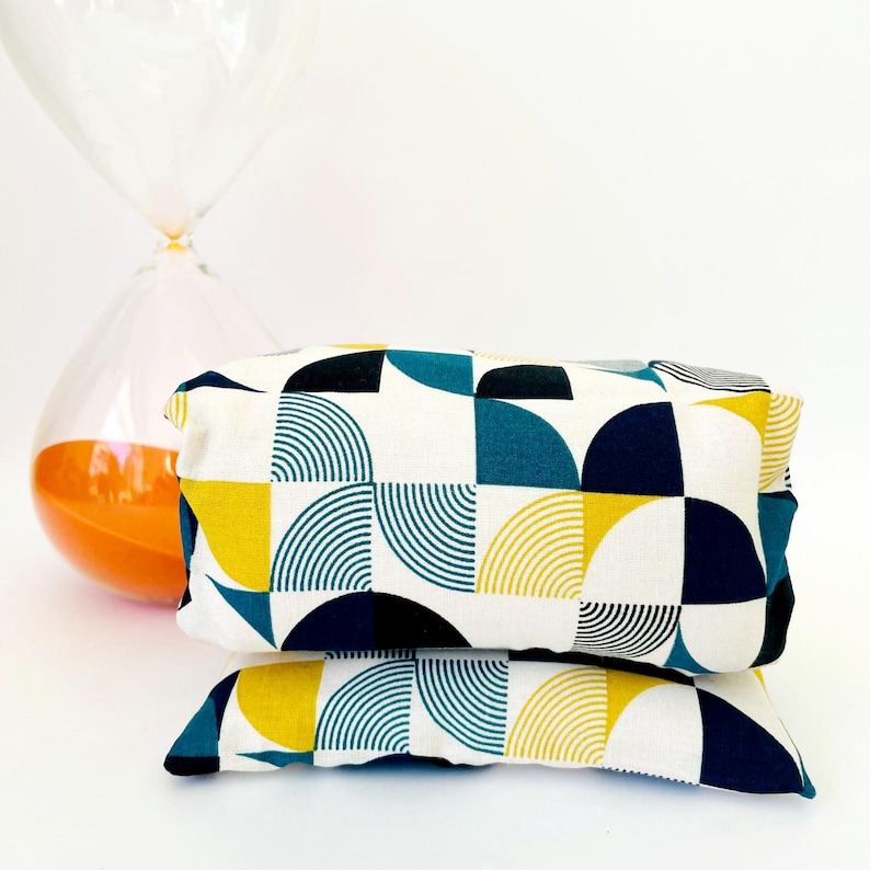 May include: Two rectangular cushions with a geometric pattern. The pattern features teal, yellow, black, and white circles and semi-circles.