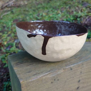 Op de afbeelding: Een kleine, witte keramische kom met een bruine glazuur aan de binnenkant en een bruin druppelontwerp aan de buitenkant.