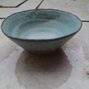 Peut inclure: Un bol en céramique bleu clair avec une surface légèrement texturée. Le bol est vide et posé sur une surface carrelée gris clair.