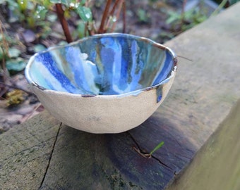 May include: A small, white ceramic bowl with blue and brown stripes. The bowl is sitting on a wooden surface.