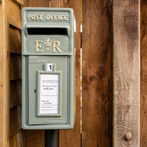 Könnte beinhalten: Ein salbeigrüner Briefkasten aus Metall mit der geprägten Aufschrift POST OFFICE und dem königlichen Monogramm E R mit Krone. Auf der Vorderseite befindet sich ein Aushang mit den Leerungszeiten: Montag bis Freitag um 16:00 Uhr und Samstag um 12:00 Uhr.