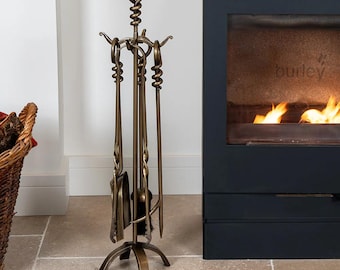 May include: A bronze fireplace tool set with a stand. The set includes a poker, shovel, brush, and tongs. The tools have decorative twisted handles and are arranged on a tripod base. The stand has a looped top. The tools are made of metal.