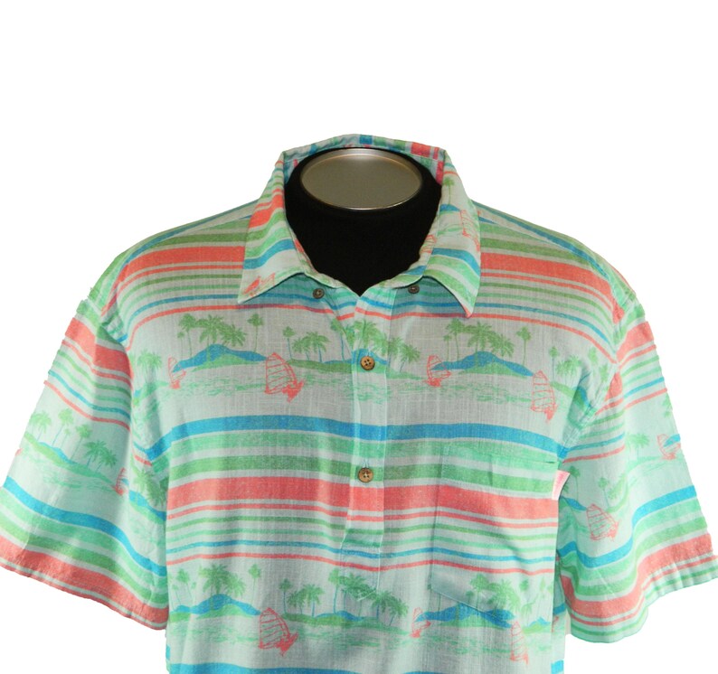 Pu&ograve; includere: Camicia a maniche corte con un design tropicale. La camicia presenta strisce orizzontali verdi, blu e corallo. Ha un colletto button-down e un motivo di palme e barche a vela.