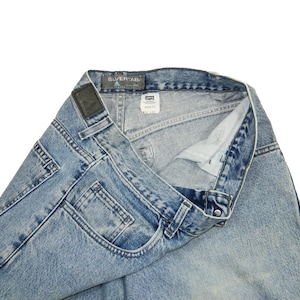 May include: Light blue denim jeans with a faded wash. The jeans feature a classic five-pocket design, belt loops, and a leather patch. The brand name "SILVERTAB" is visible on the back. The jeans are folded, showcasing the interior and label.