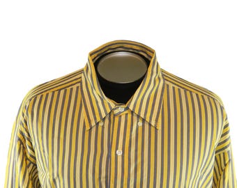 Puede incluir: Camisa a rayas amarillas y azul marino con cuello clásico y mangas largas. Un pequeño logotipo azul es visible en el pecho. La camisa se exhibe en un maniquí.