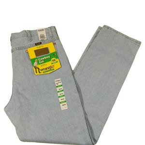 Op de afbeelding: Lichtblauwe spijkerbroek met een Wrangler Cowboy Cut-label. Het label is groen en geel met het Wrangler-logo en de woorden "Cowboy Cut" en "936".