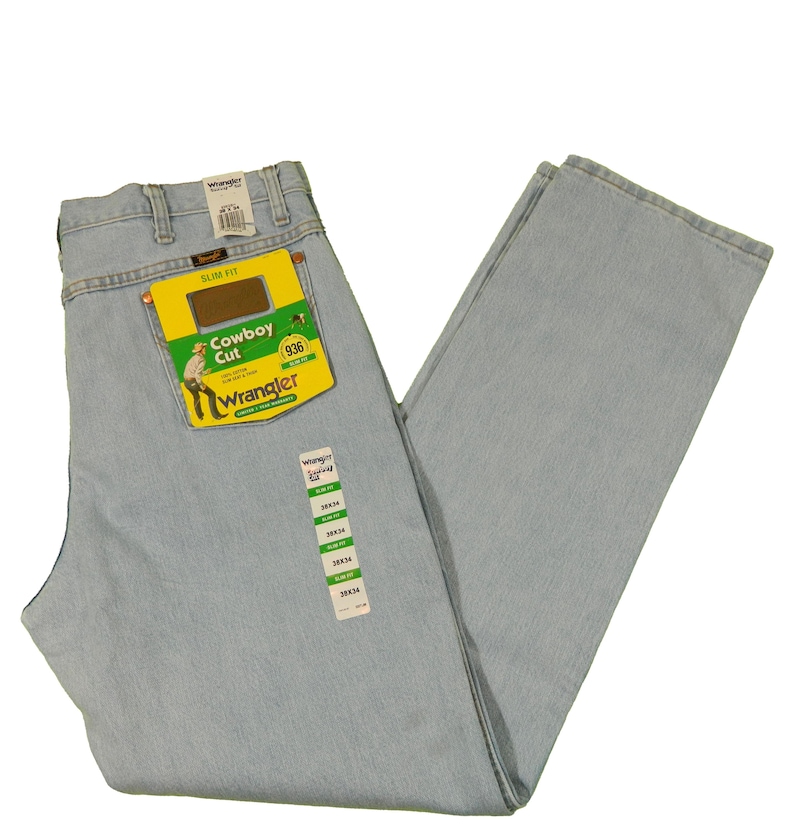 Op de afbeelding: Lichtblauwe spijkerbroek met een Wrangler Cowboy Cut-label. Het label is groen en geel met het Wrangler-logo en de woorden "Cowboy Cut" en "936".