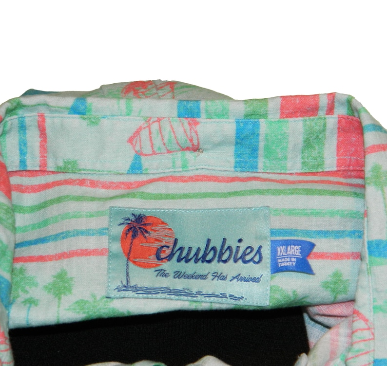 Pu&ograve; includere: Camicia azzurra con bottoni e motivo a righe colorate in rosso, verde e blu. La camicia presenta una toppa con la scritta "chubbies" e la frase "The Weekend Has Arrived!" ed &egrave; taglia XXL.