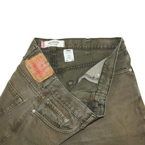 May include: Olive green Levi's 550 relaxed fit jeans with a tan leather patch on the back waistband. The interior features a white care tag with text including W38 L32 and a white label reading Relaxed Fit 550 Jeans. Metal rivets are visible.