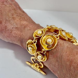 May include: A gold-tone bracelet with a toggle clasp. The bracelet is made of linked, overlapping circles with faux pearls set in each circle.