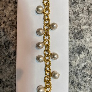 May include: Gold-toned bracelet featuring a chain design with alternating links and faux pearl accents. The bracelet has a toggle clasp closure. The pearls are a light, off-white color. The bracelet is displayed on a white background.
