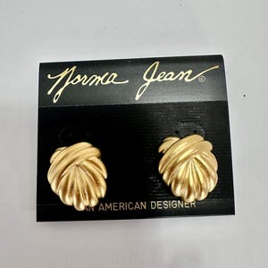 May include: Gold-toned Norma Jean earrings on a black card. The earrings have a textured, knotted design. The card features the brand name in gold script and the text "AN AMERICAN DESIGNER".
