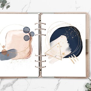 May include: Two pages of a planner with abstract watercolor designs in shades of pink, blue, and gold. The designs include circles, squares, and triangles.