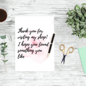 May include: A white card with the text "Thank you for visiting my shop! I hope you found something you like" on a white wooden background with a cup of coffee, a plant, a notebook, and a pair of scissors.