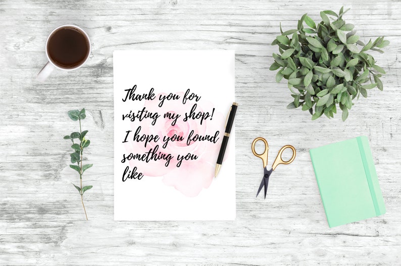 May include: A white card with the text "Thank you for visiting my shop! I hope you found something you like" on a white wooden background with a cup of coffee, a plant, a notebook, and a pair of scissors.