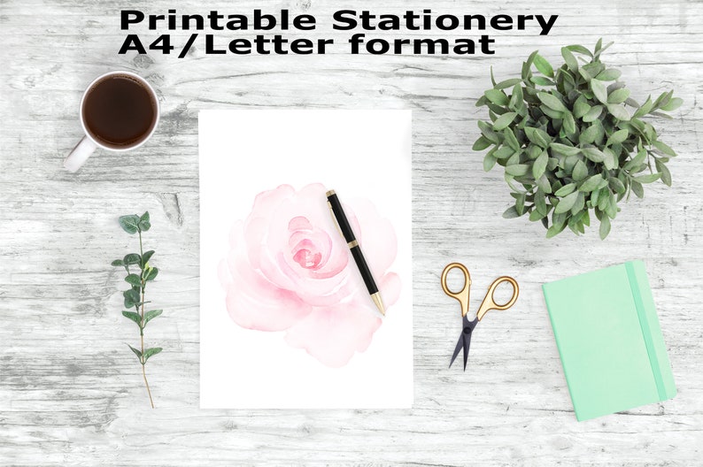 May include: Printable stationery in A4/Letter format featuring a watercolor pink rose with a black pen on a white background. The stationery is surrounded by a wooden surface with a green plant, a cup of coffee, and gold scissors.