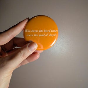 May include: A round, orange button with the white text: "Who knew the hard times were the good ol' days?" The button has a glossy finish.