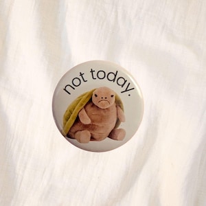 Könnte beinhalten: Ein runder Button mit dem Text "not today" und einer Cartoon-Schildkröte mit traurigem Gesichtsausdruck und gelber Decke. Der Hintergrund ist weiß.