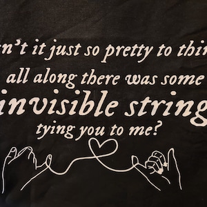 Könnte beinhalten: Schwarzer Stoff mit weißem Text, der lautet: "isn't it just so pretty to think all along there was some invisible string tying you to me?"  Zwei Hände sind mit einem weißen Faden verbunden.