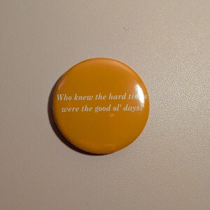 K&ouml;nnte beinhalten: Ein runder, orangefarbener Button mit dem wei&szlig;en Text: "Who knew the hard times were the good ol' days?". Der Button hat eine gl&auml;nzende Oberfl&auml;che und der Text ist zentriert. Der Button hat eine einfarbige orange Farbe.