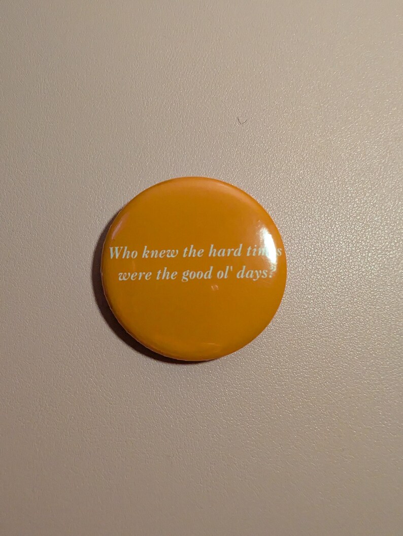 K&ouml;nnte beinhalten: Ein runder, orangefarbener Button mit dem wei&szlig;en Text: "Who knew the hard times were the good ol' days?". Der Button hat eine gl&auml;nzende Oberfl&auml;che und der Text ist zentriert. Der Button hat eine einfarbige orange Farbe.