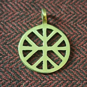 May include: A gold-colored metal pendant with a circular design featuring a wheel with eight spokes. The pendant has a loop at the top for attaching to a chain.