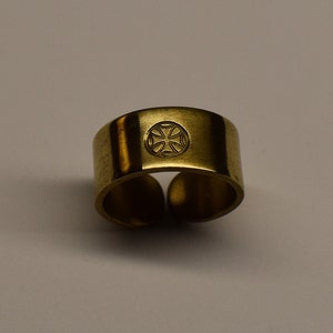 Könnte beinhalten: Ein goldfarbener Metallring mit einem eingravierten Kreuzmuster auf der Oberseite.