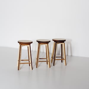 May include: Three wooden bar stools with a light brown finish and a natural wood top. The stools have a simple, modern design with a square frame and a round seat.