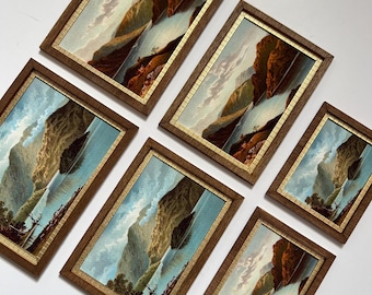 May include: A collection of six rectangular framed wall art pieces featuring identical landscape prints of mountains, a body of water, and trees. Each print is encased in a brown wooden frame with a thin gold inner border, arranged in a cluster.