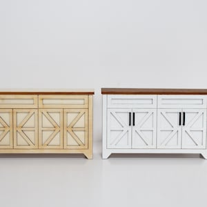 May include: Two miniature wooden cabinets. One is light beige with a natural wood top, the other is white with a dark brown top. Both have geometric door designs and black hardware.