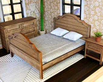 May include: A wooden bed frame with a headboard and footboard, a white and gray striped bedspread, two white pillows, and a wooden nightstand with a drawer. The bed is in a room with a wooden dresser and a potted plant.