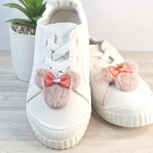 Puede incluir: Zapatillas de lona blancas con cordones blancos. Cada zapato presenta un lazo rosa con un dise&ntilde;o de personaje de dibujos animados. Los zapatos tienen suela de goma y son adecuados para uso casual.