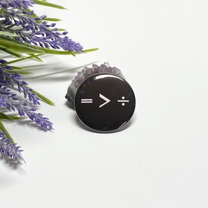 May include: A black button with a white symbol that reads "= > ÷" on it.