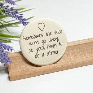 May include: White round ceramic coaster with a heart and the text "Sometimes the fear won't go away, so you'll have to do it afraid."