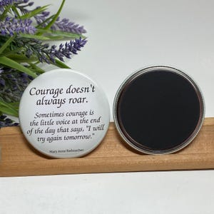 May include: White round magnet with the quote "Courage doesn't always roar. Sometimes courage is the little voice at the end of the day that says, 'I will try again tomorrow.'" by Mary Anne Radmacher.